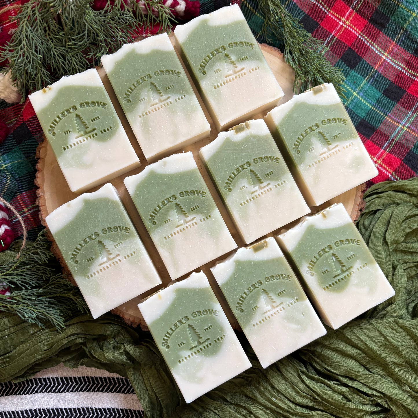 Assorted green and beige soaps with a brand logo on a plaid fabric background