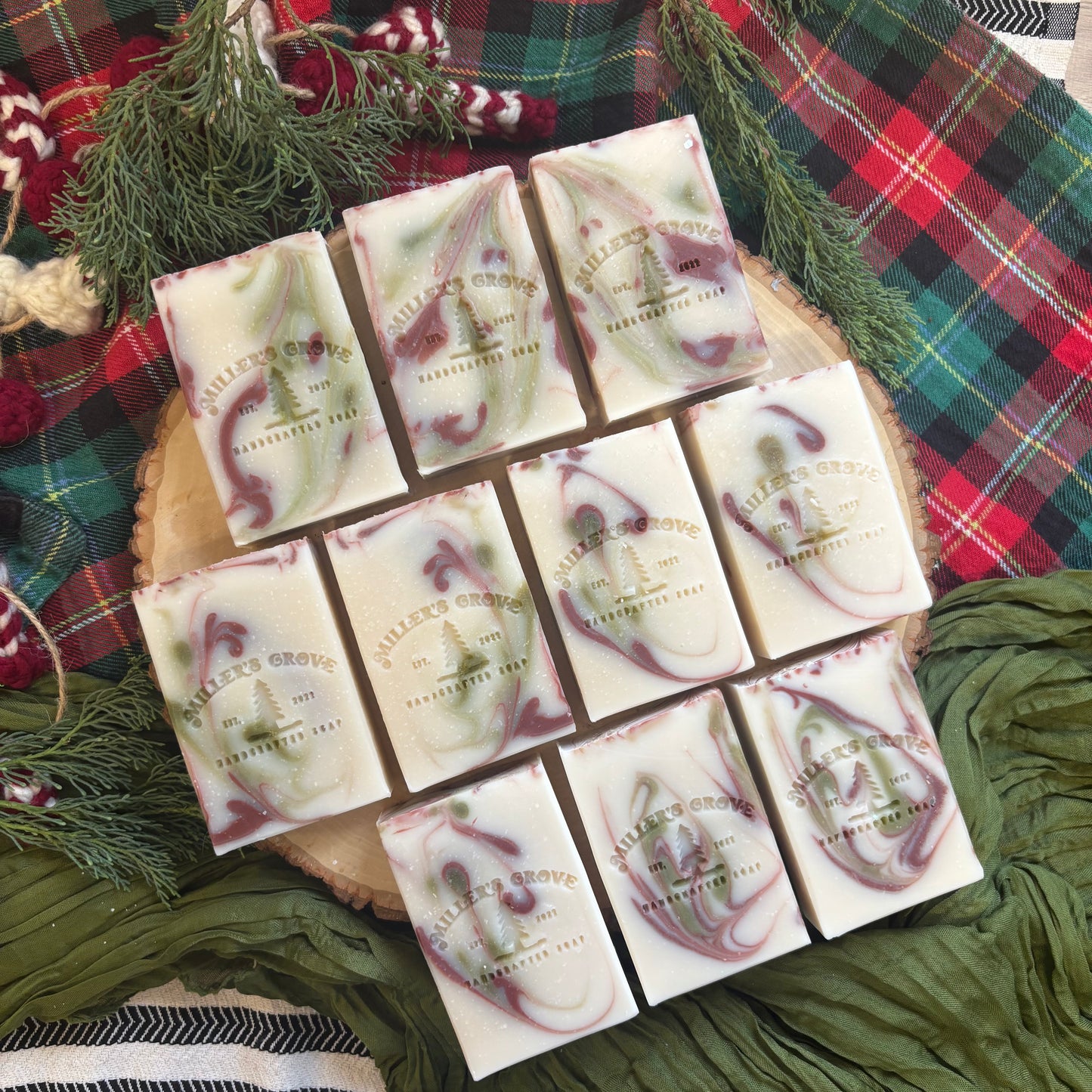 Assorted soap bars with a brand logo on a wooden board against a plaid fabric background.
