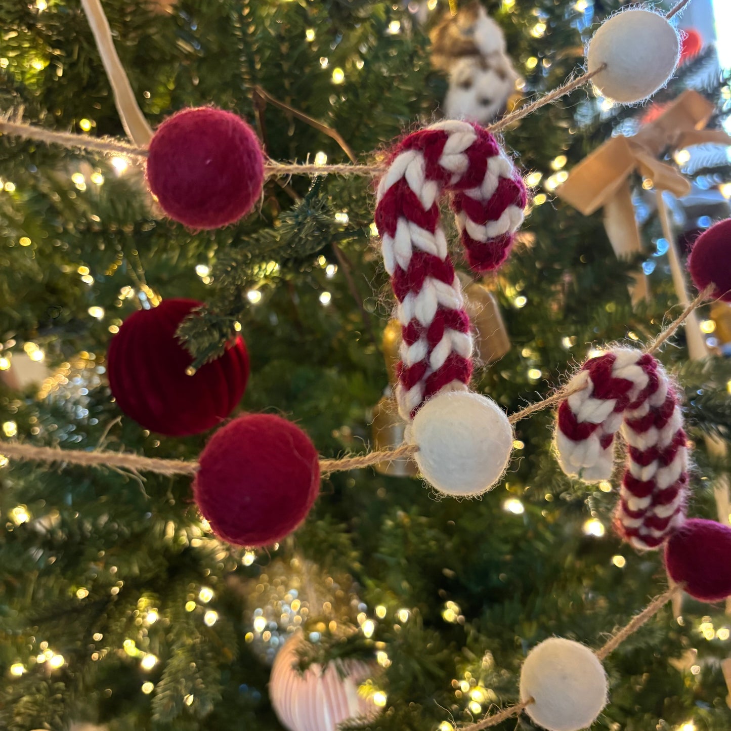 Decorative candy cane and ball ornaments on a Christmas tree with blurred lights in the background.