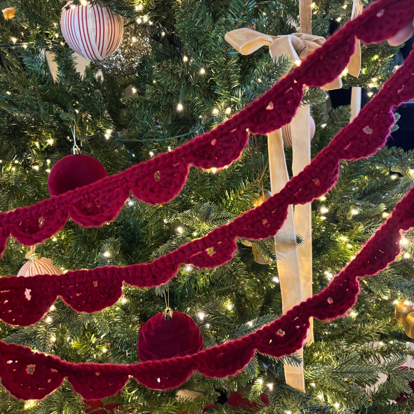 Red crochet garland on a decorated Christmas tree with lights and ornaments.