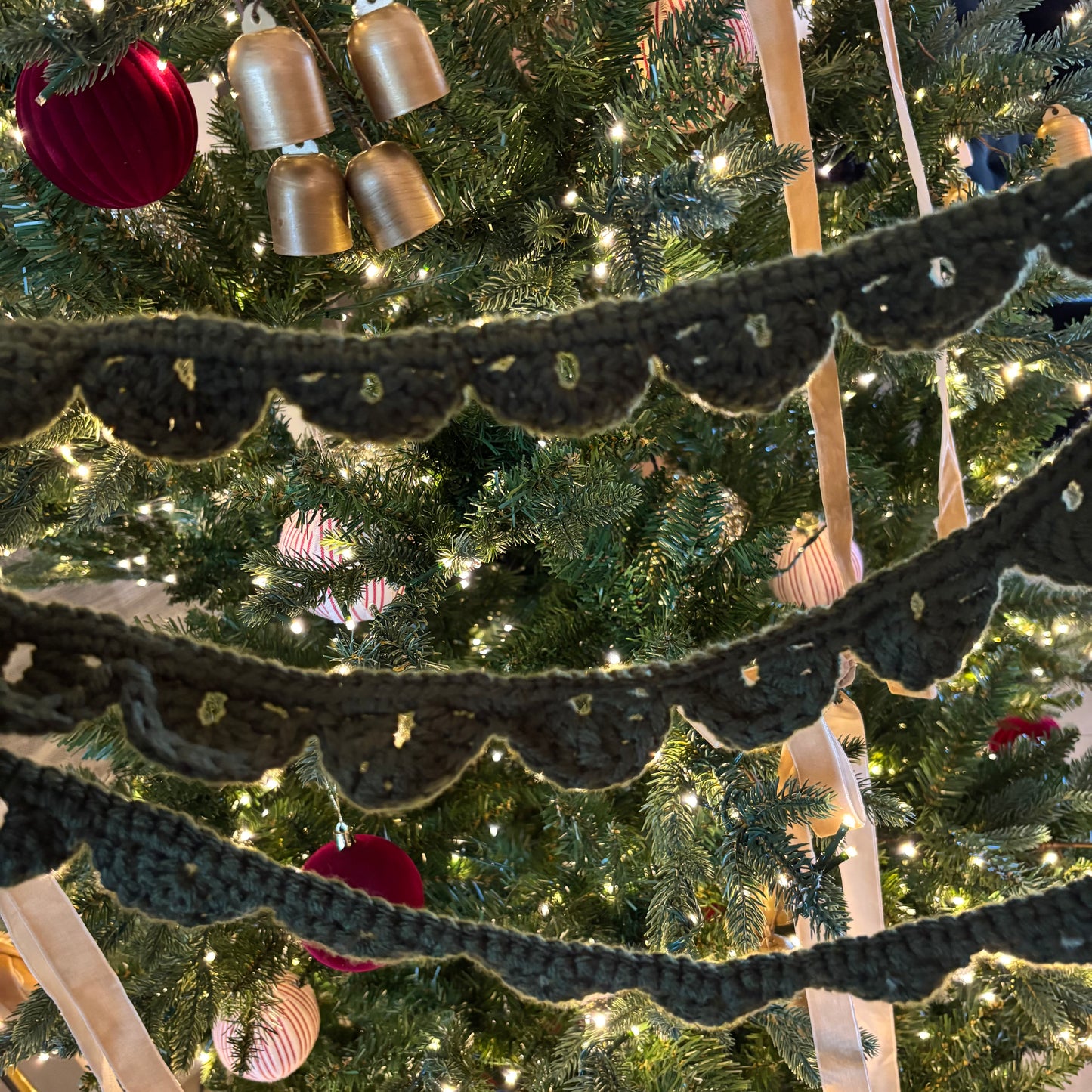 Close-up of a Christmas tree with lights, ornaments, and a knitted garland.