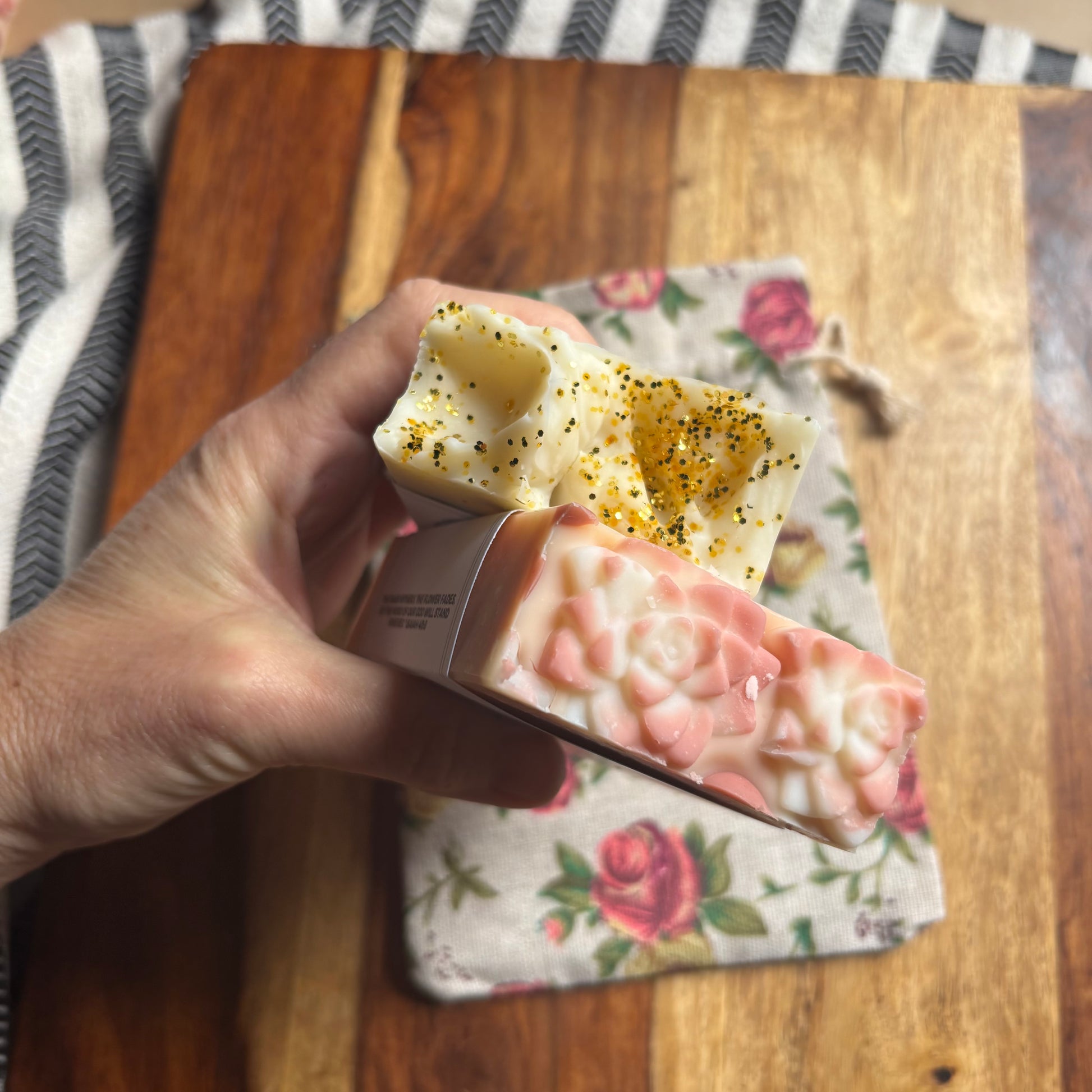 Hand holding a bar of soap wrapped in a floral-patterned cloth on a wooden surface.