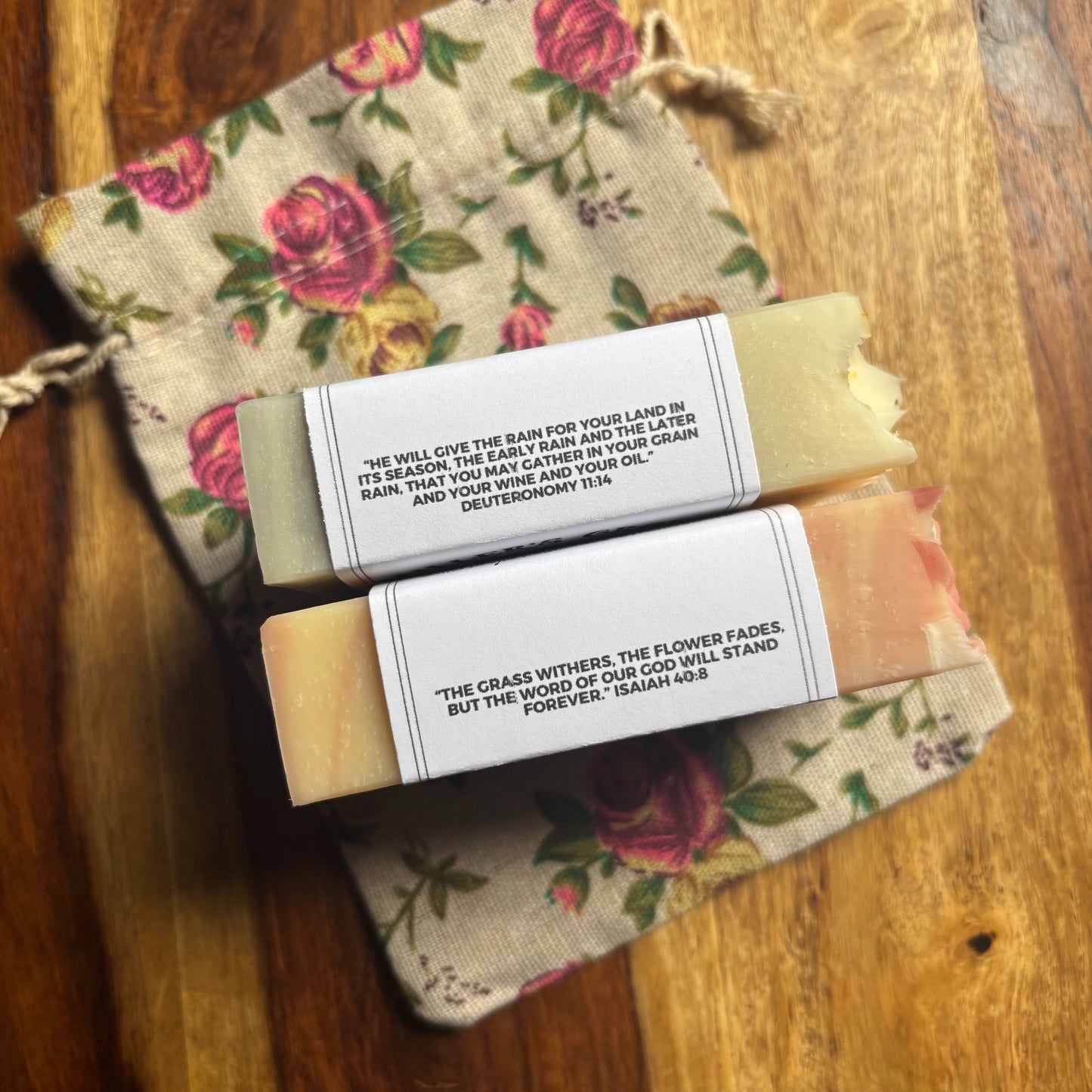 Two bars of soap with biblical text on a floral-patterned bag on a wooden surface