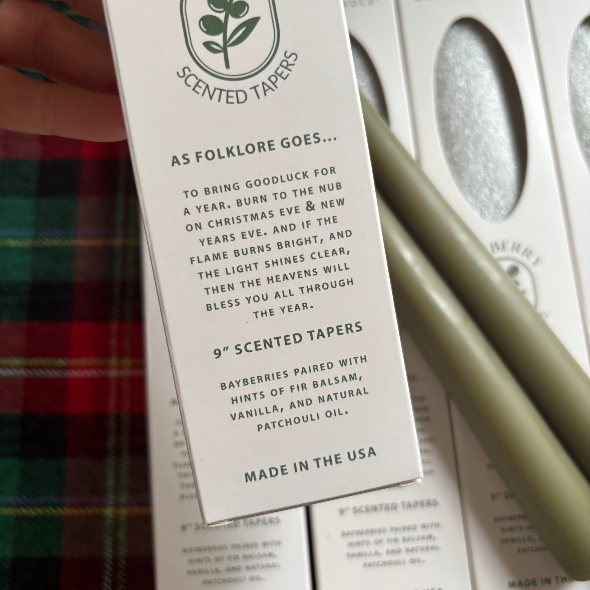 Scented taper packaging with text and a candle on a plaid fabric background