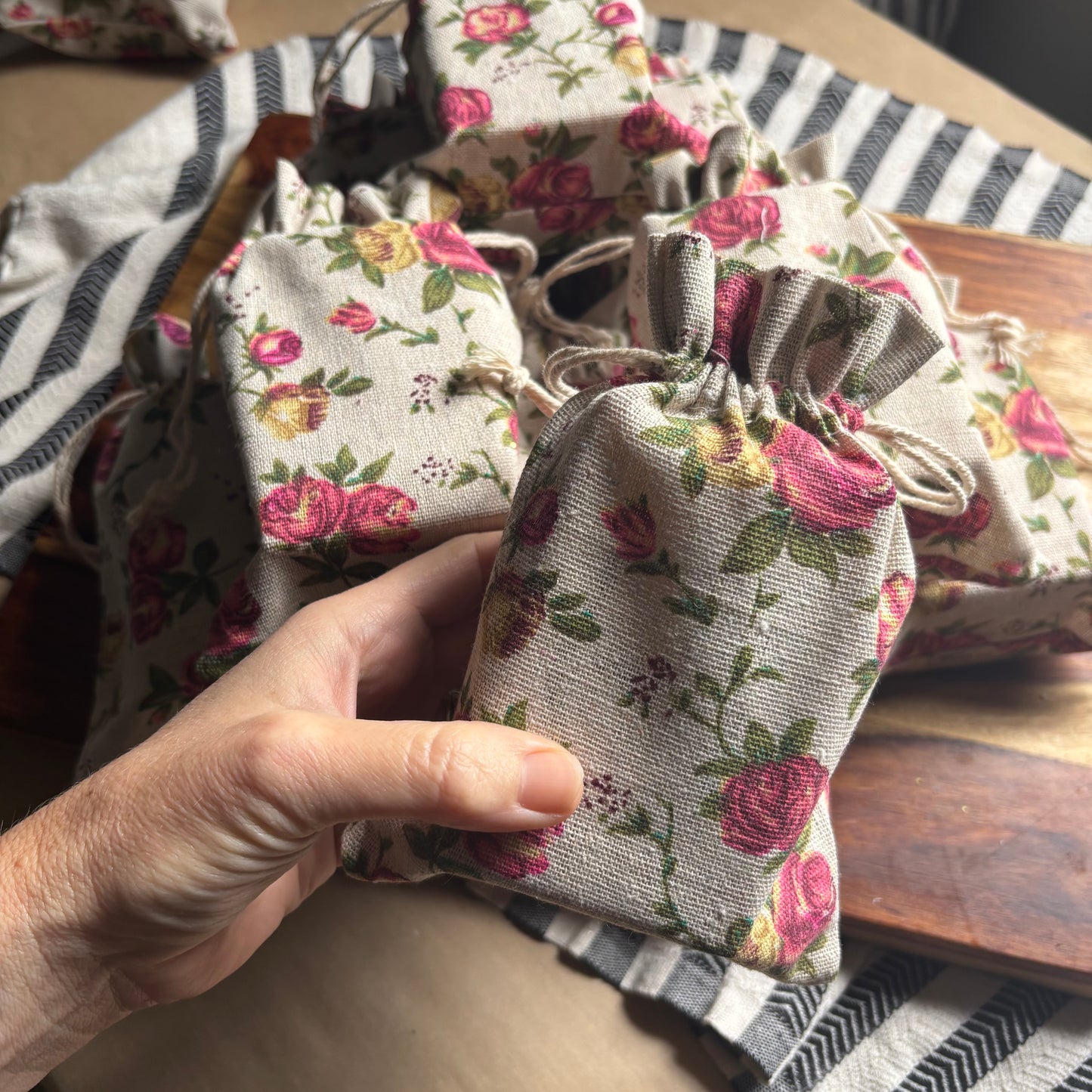 Hand holding a small floral fabric pouch on a wooden surface with more pouches in the background.
