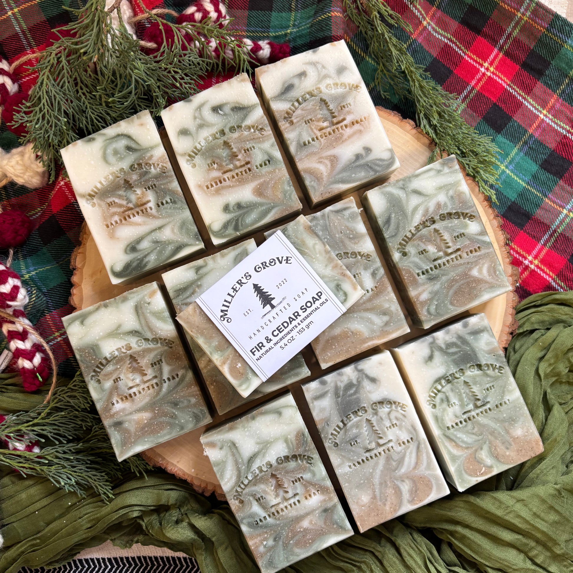 Marble-patterned soap bars on a wooden board with a 'Millers Grove' label, surrounded by greenery and plaid fabric.