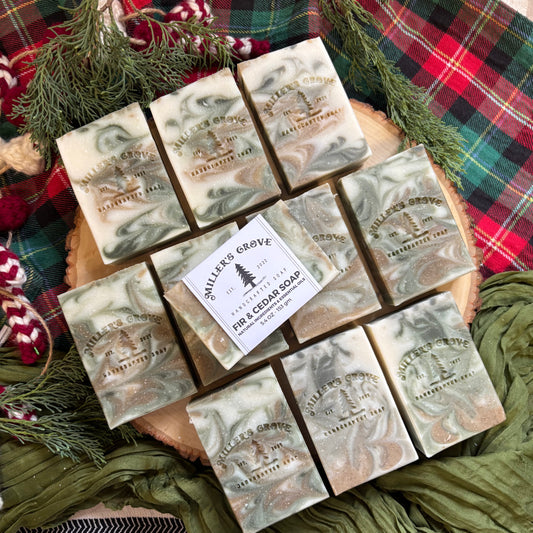 Marble-patterned soap bars on a wooden board with a 'Millers Grove' label, surrounded by greenery and plaid fabric.