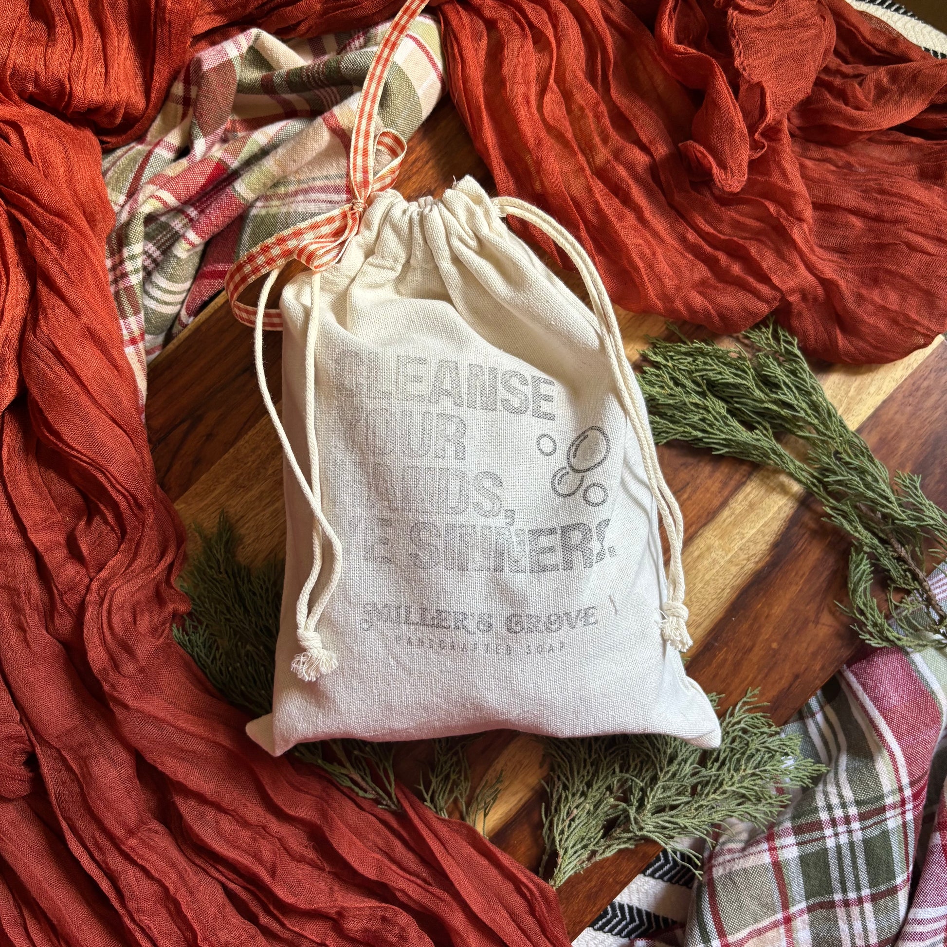 White drawstring bag with text on a wooden surface with red and plaid fabric in the background