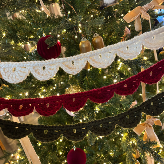 Decorative crochet garlands in white, red, and black hanging on a Christmas tree.