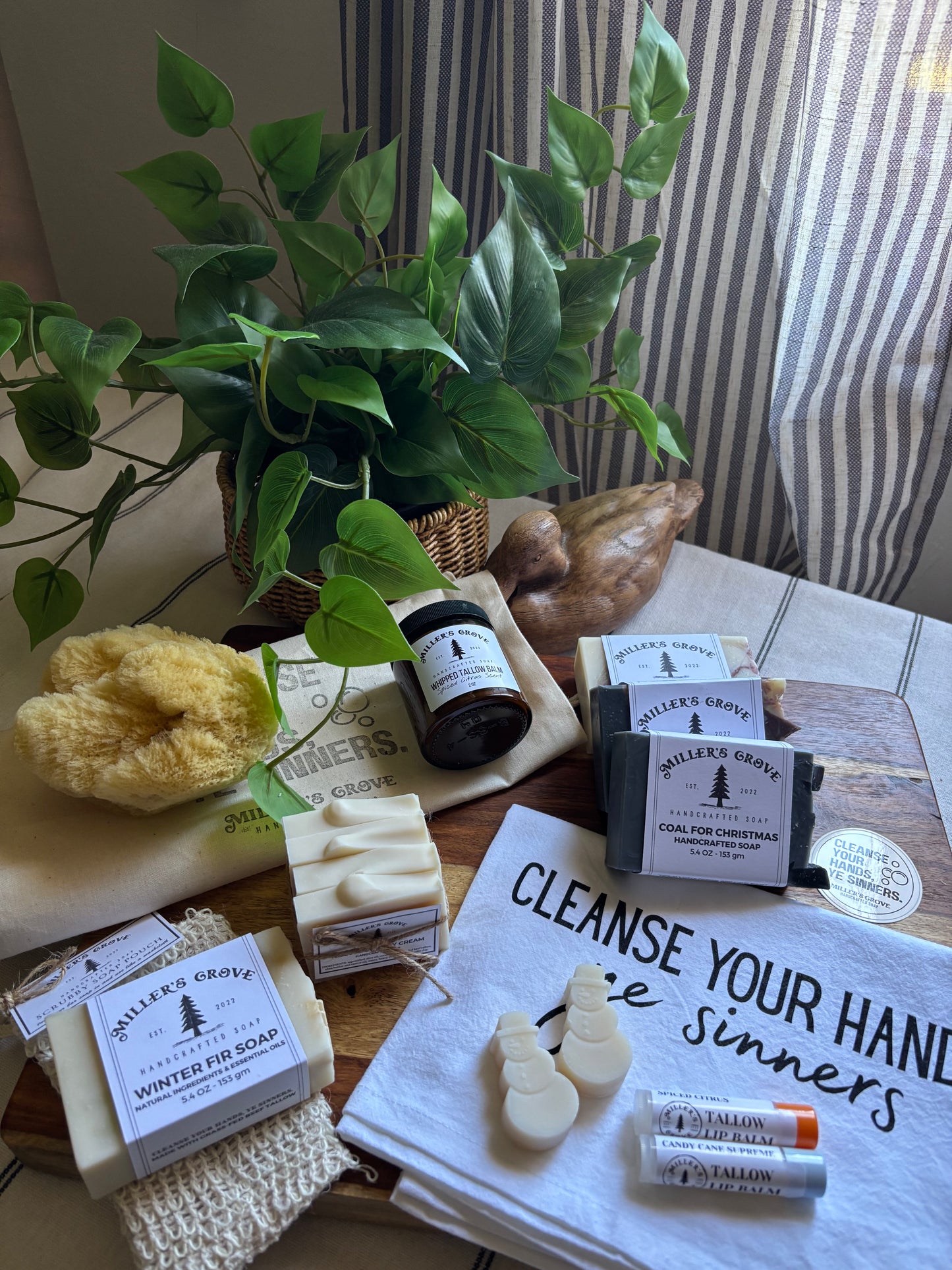 Collection of natural products including soap, candles, and a plant on a table with a humorous sign.