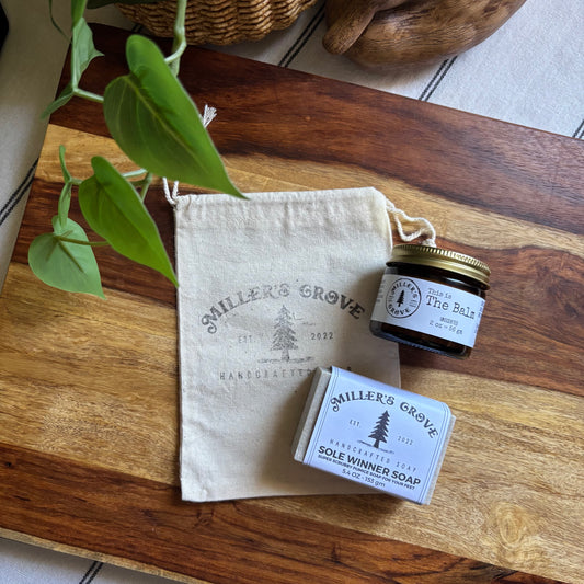 Small jar, bar of soap, and cloth bag labeled 'Miller's Grove' on a wooden surface.