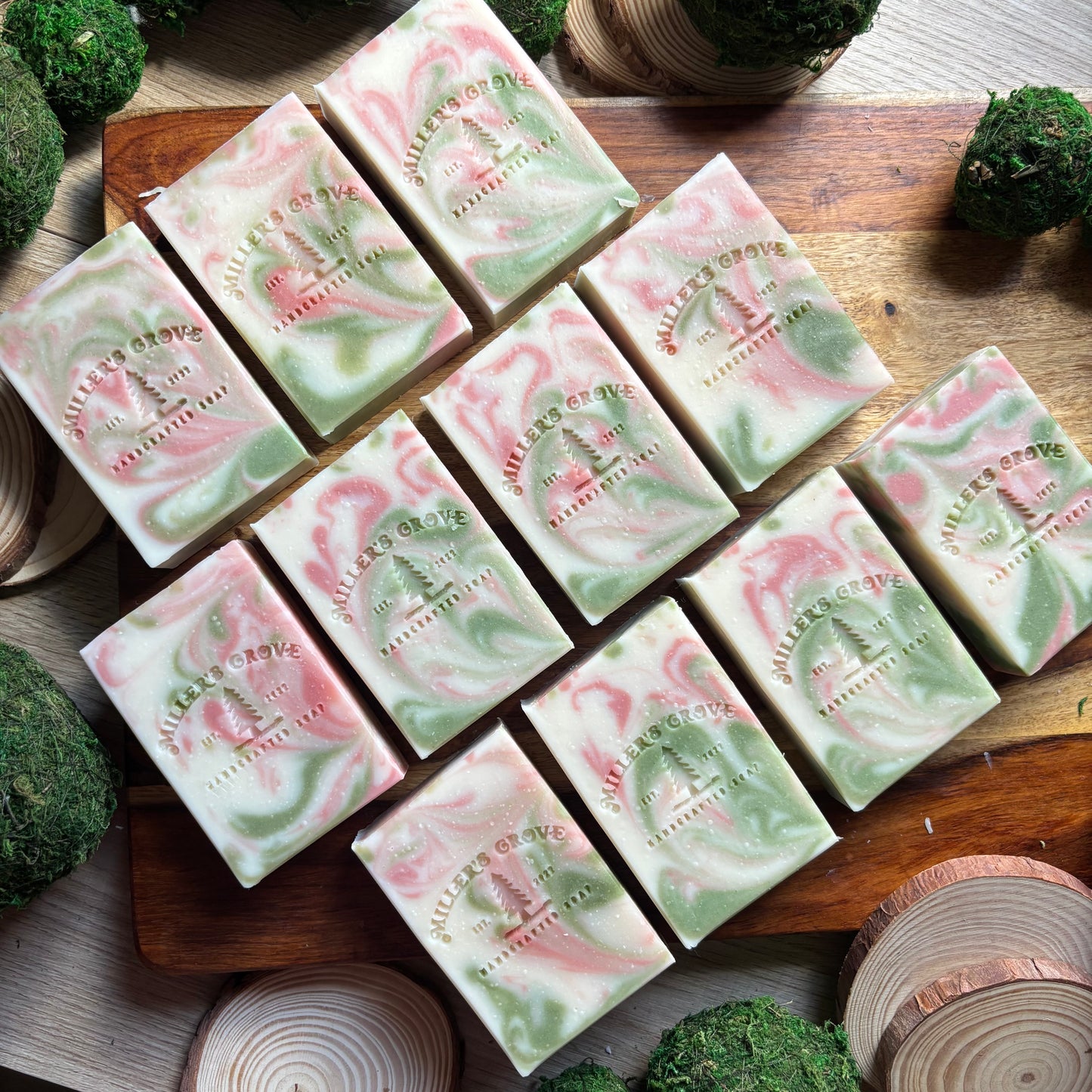 Green and pink marbled soap bars on a wooden cutting board with decorative elements.