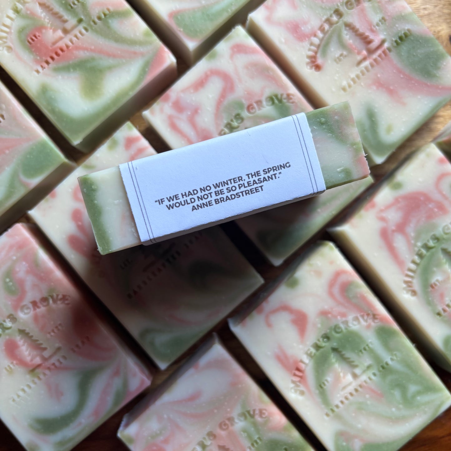 Handmade soap bars with a central bar featuring a quote, surrounded by others on a wooden surface.