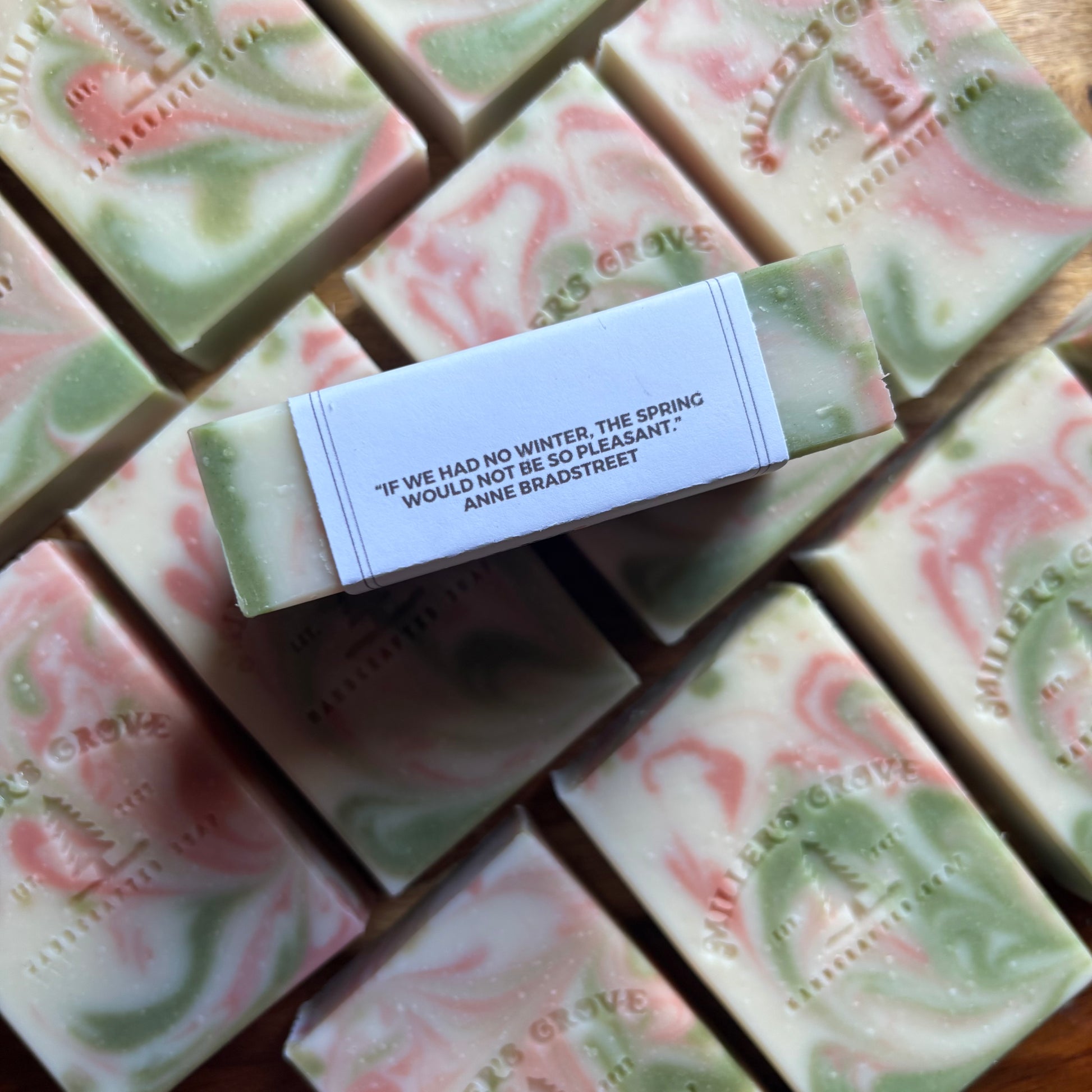 Handmade soap bars with a central bar featuring a quote, surrounded by others on a wooden surface.