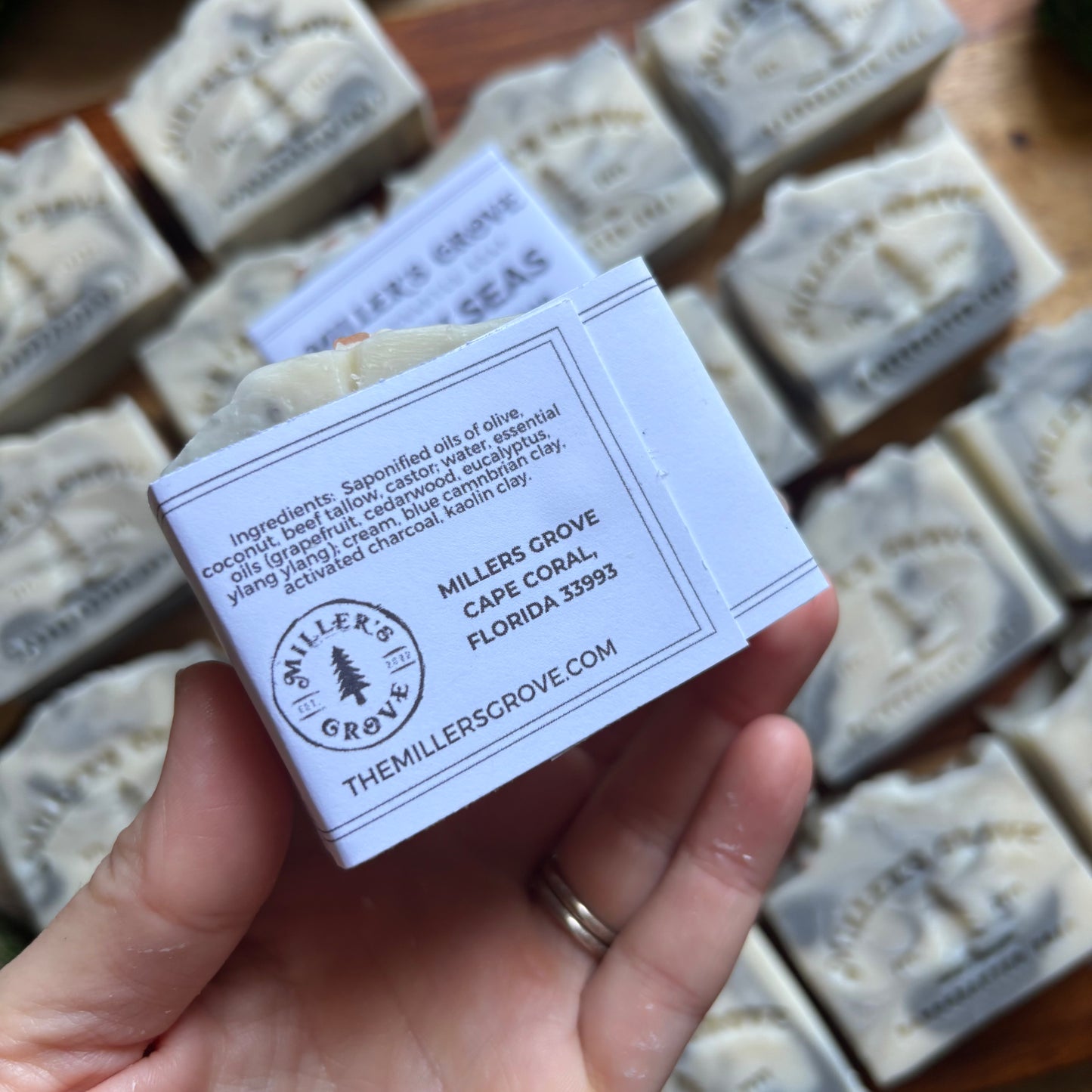 Hand holding a bar of soap with 'Miller's Grove' label, surrounded by more soap bars.