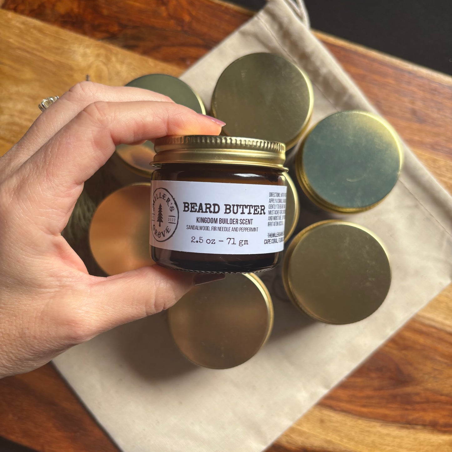 Hand holding a jar of beard butter with gold lid on a wooden surface