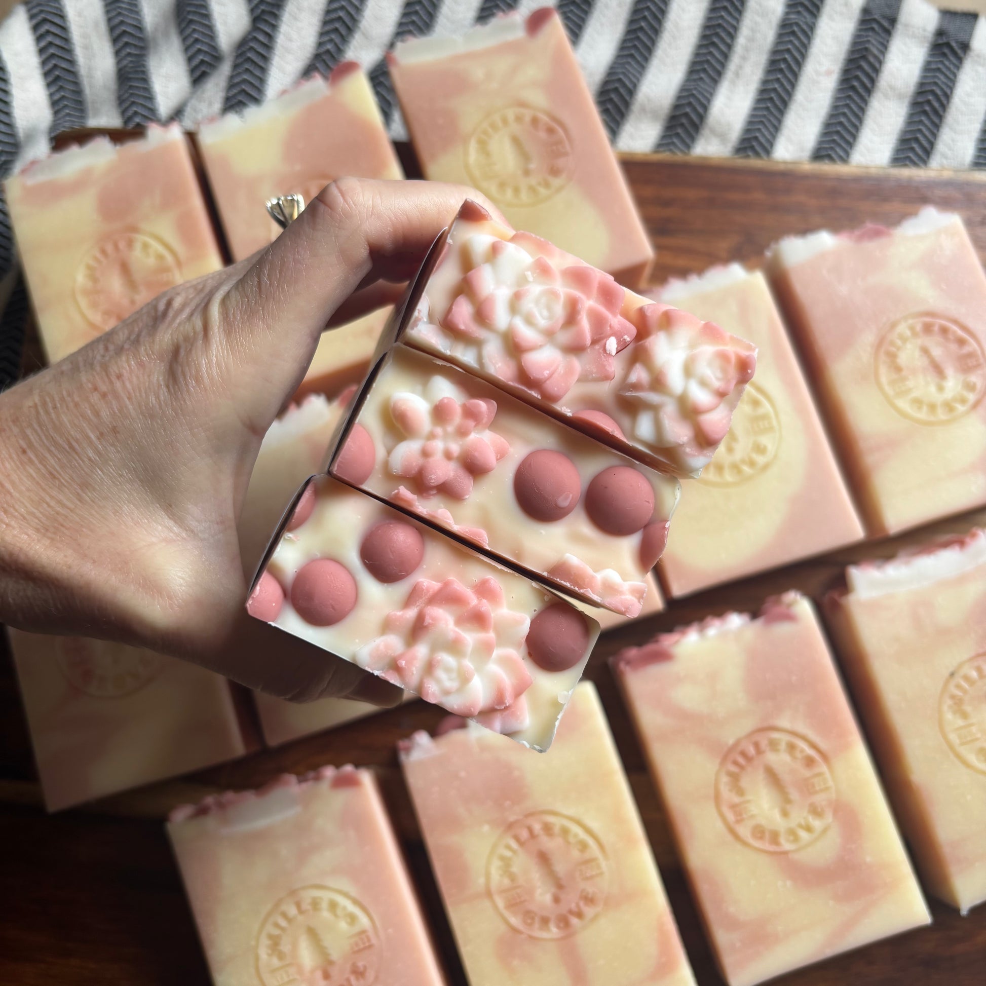 Hand holding a floral soap bar with more soap bars in the background on a striped surface