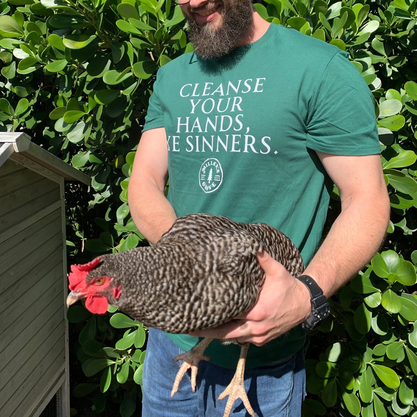 Green short sleeve t shirt that says "cleanse your hands, ye sinners".  Man wearing the shirt is holding a chicken.  
