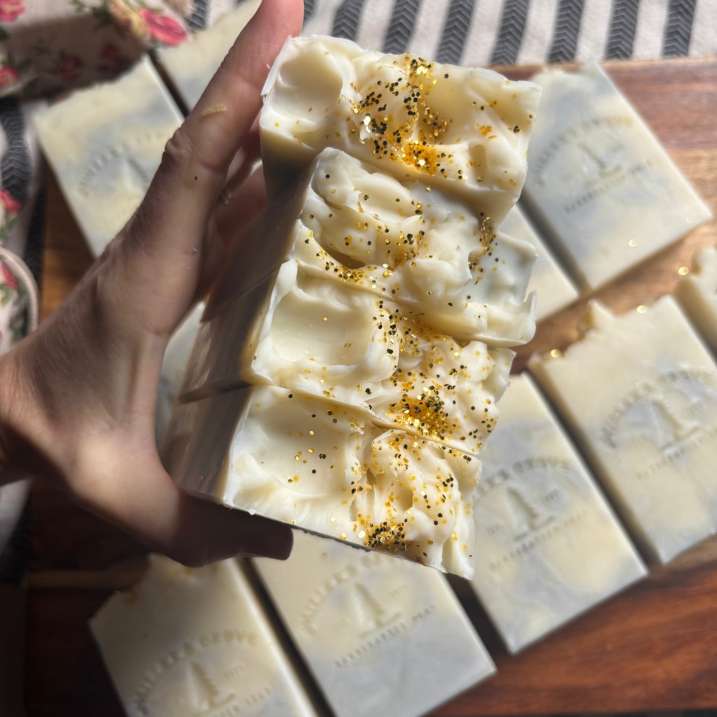 Hand holding a block of white soap with specks on a wooden surface
