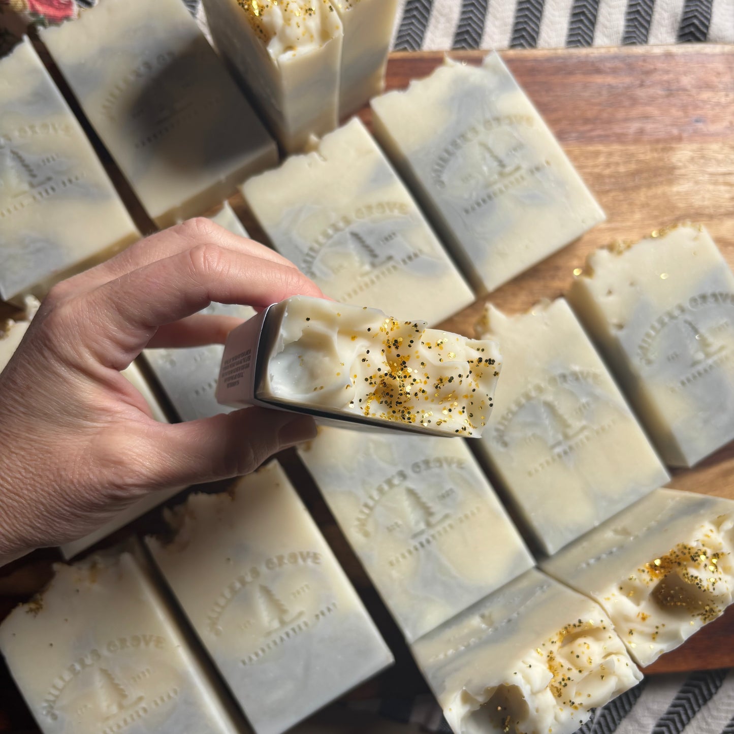 Hand holding a bar of soap with decorative elements on a wooden board with more soap bars.