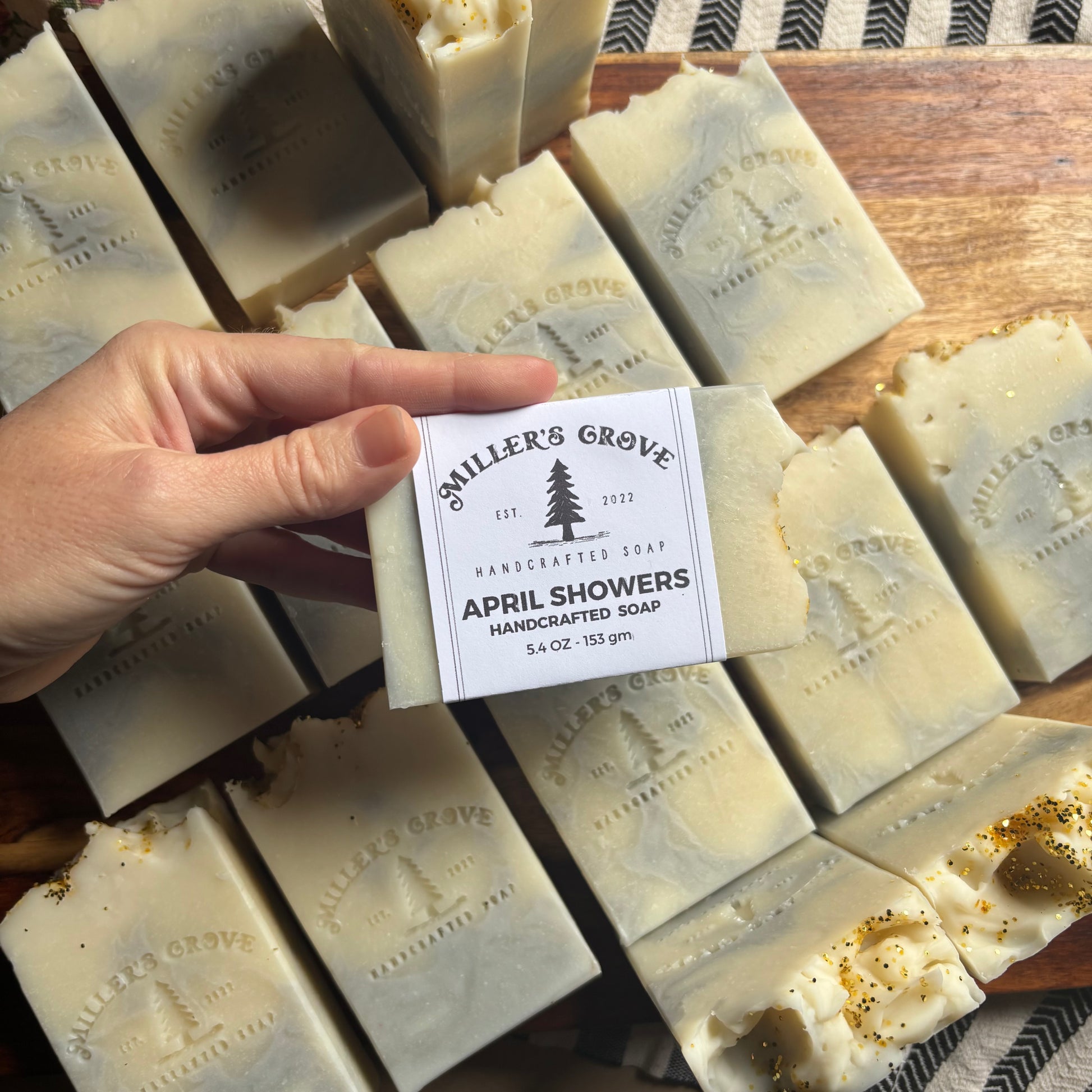 Hand holding a soap bar labeled 'Miller's Grove April Showers' among other soap bars.