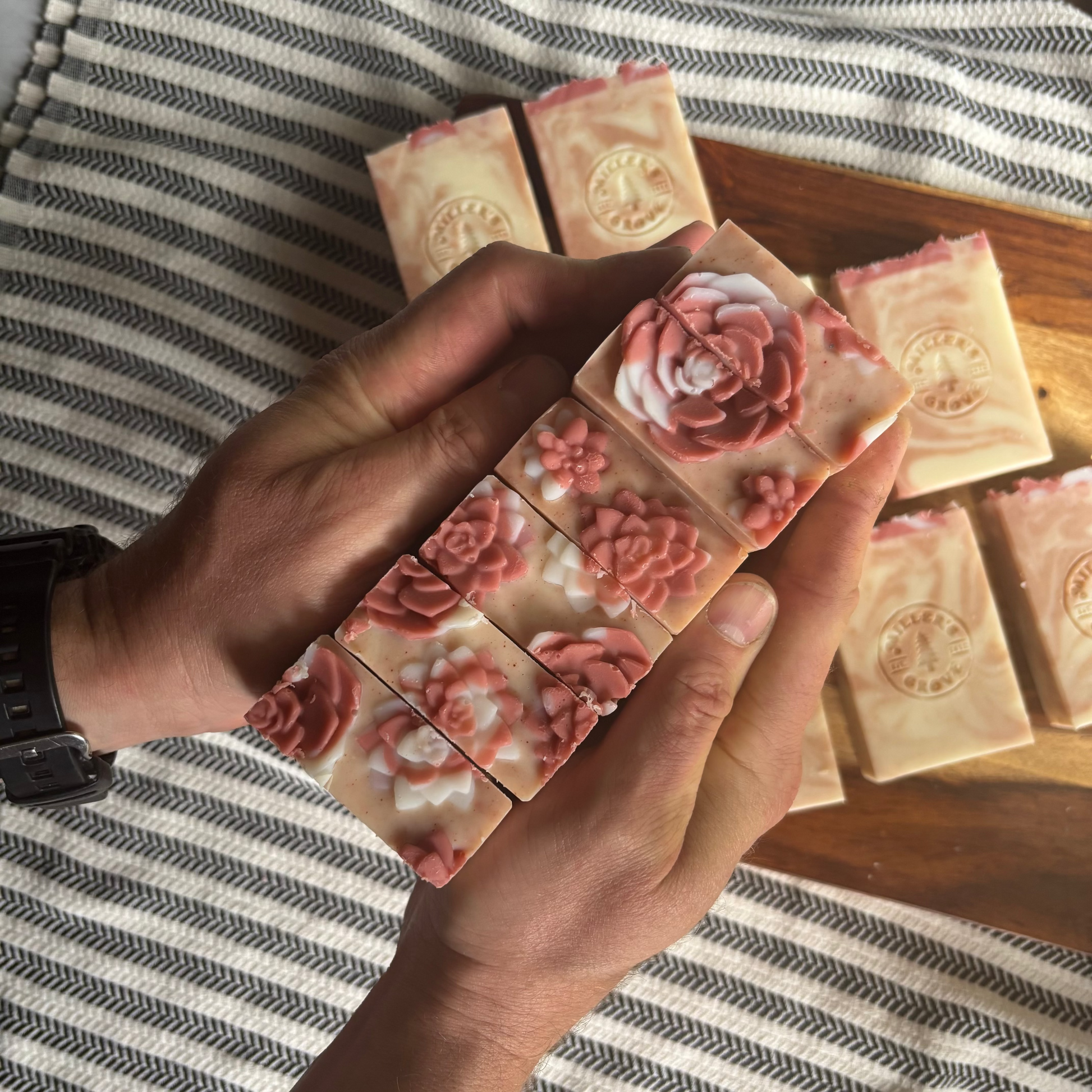 Handmade soap bars with floral designs held by a person on a striped fabric background
