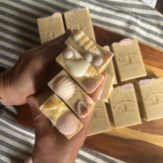 Handmade soap bars with shell designs held by a person, on a wooden surface.