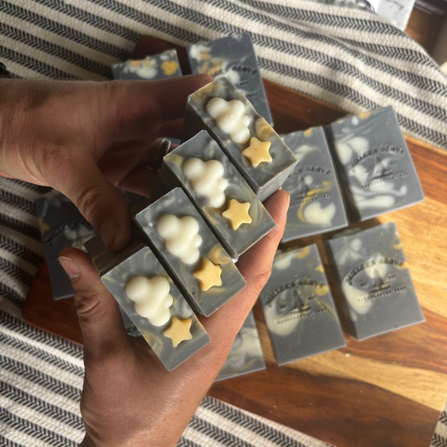 Hand holding a set of soap bars with star and cloud designs on a wooden surface.