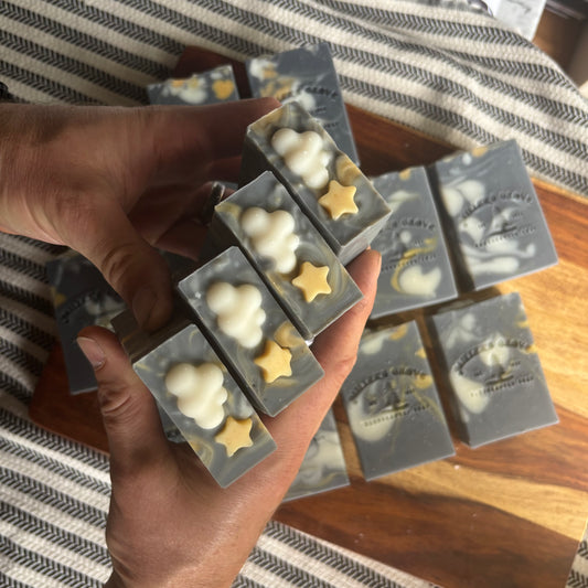 Hand holding a set of soap bars with star and cloud designs on a wooden surface.