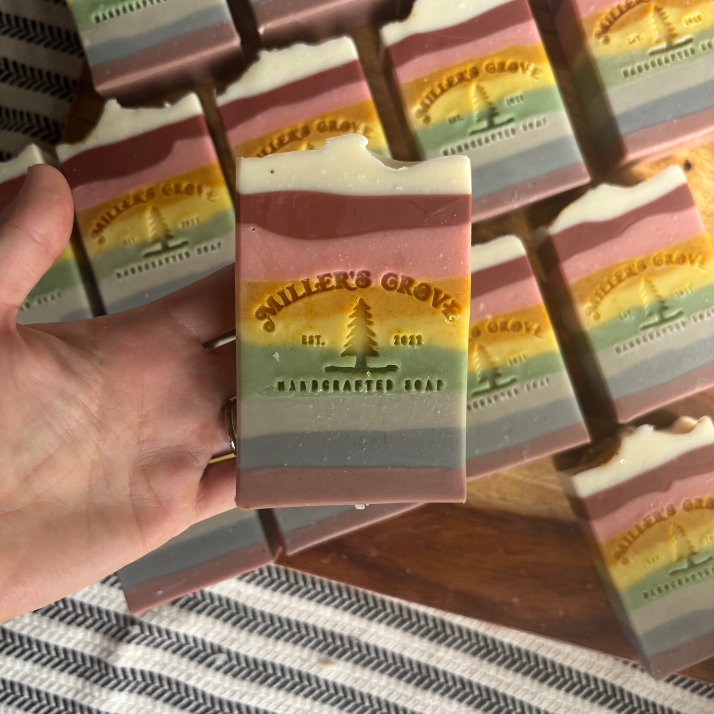 Hand holding a layered soap bar with 'Miller's Grove' branding on a striped surface.