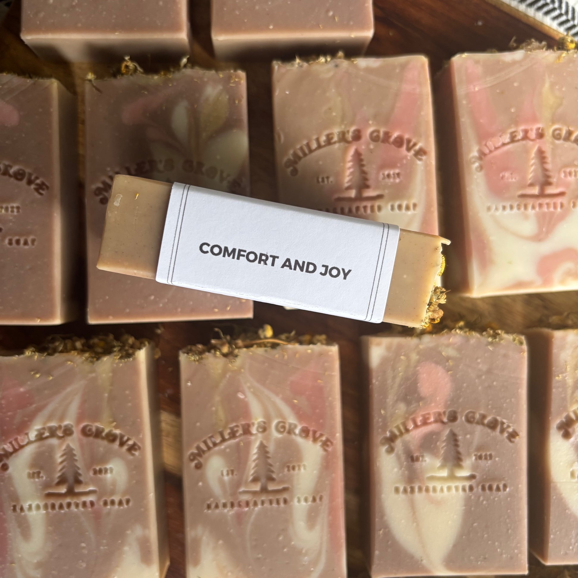 Bars of soap with 'Miller's Grove' branding and a label reading 'Comfort and Joy' on a wooden background.