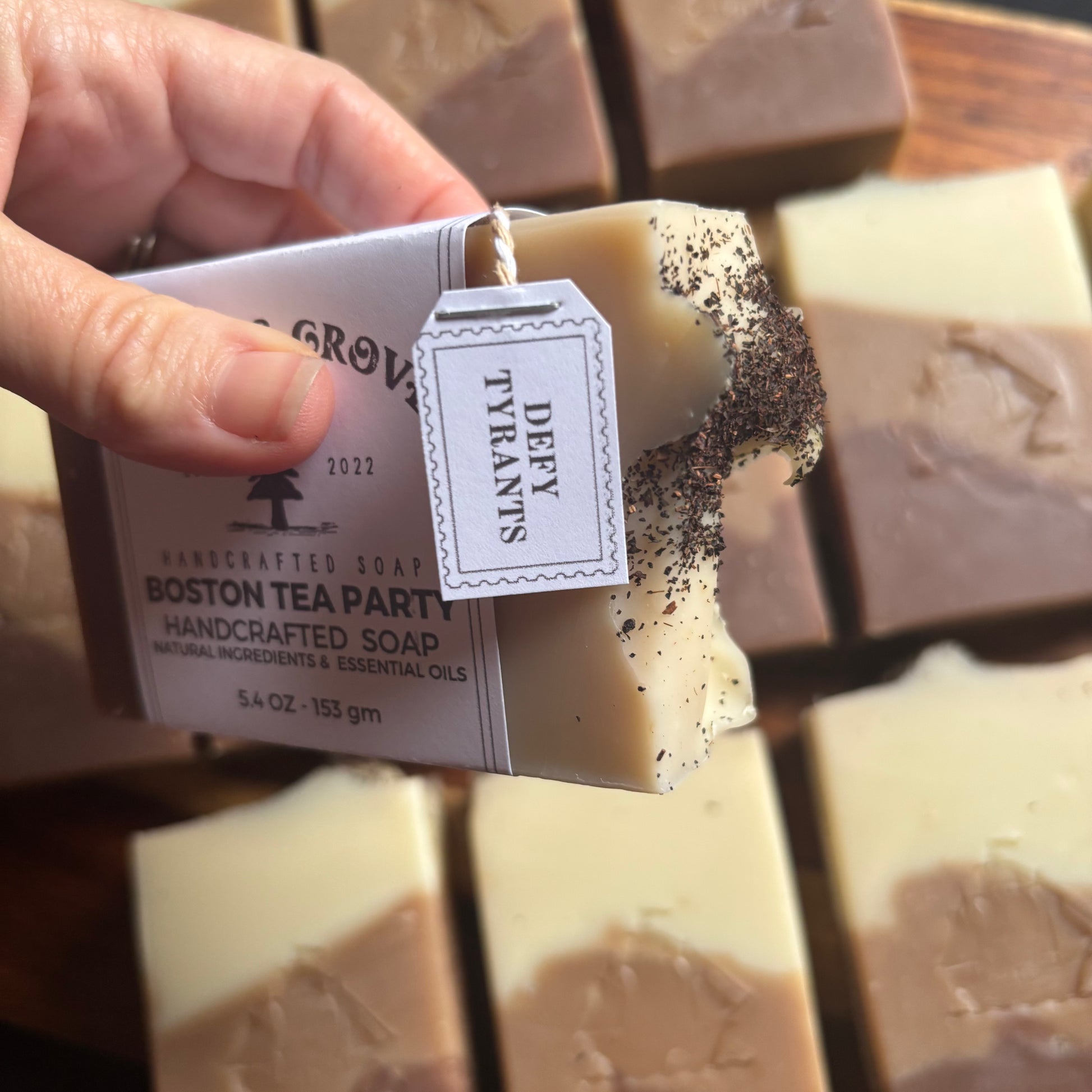Handcrafted soap with a visible label held by a hand, surrounded by more soaps on a wooden surface.