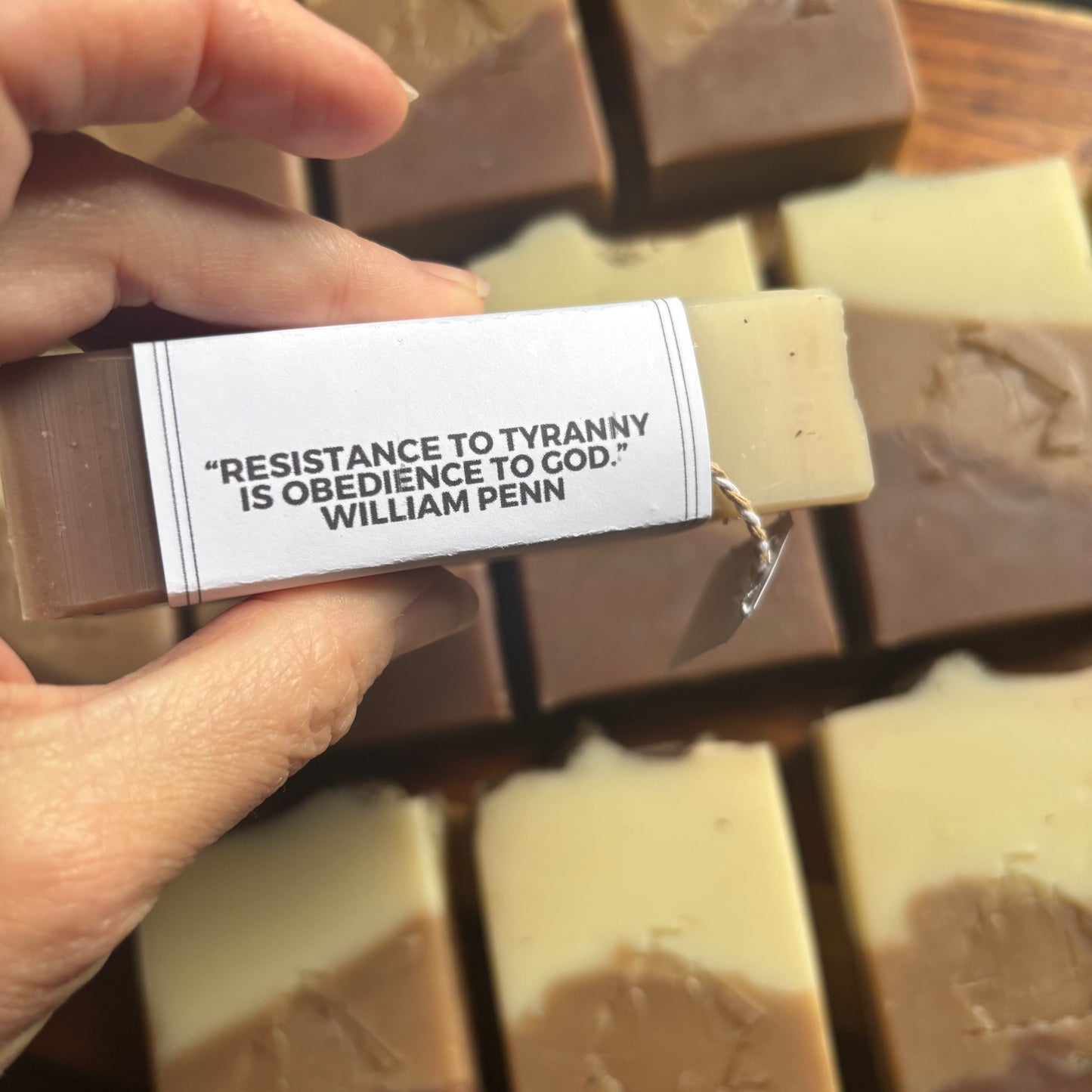 Bar of soap with a quote label held by a hand, surrounded by more soap bars.