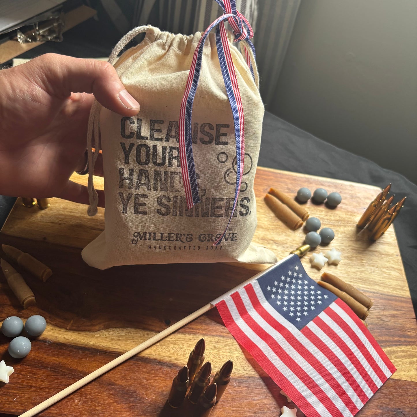 Hand holding a drawstring bag with text on a wooden surface with an American flag and various items.