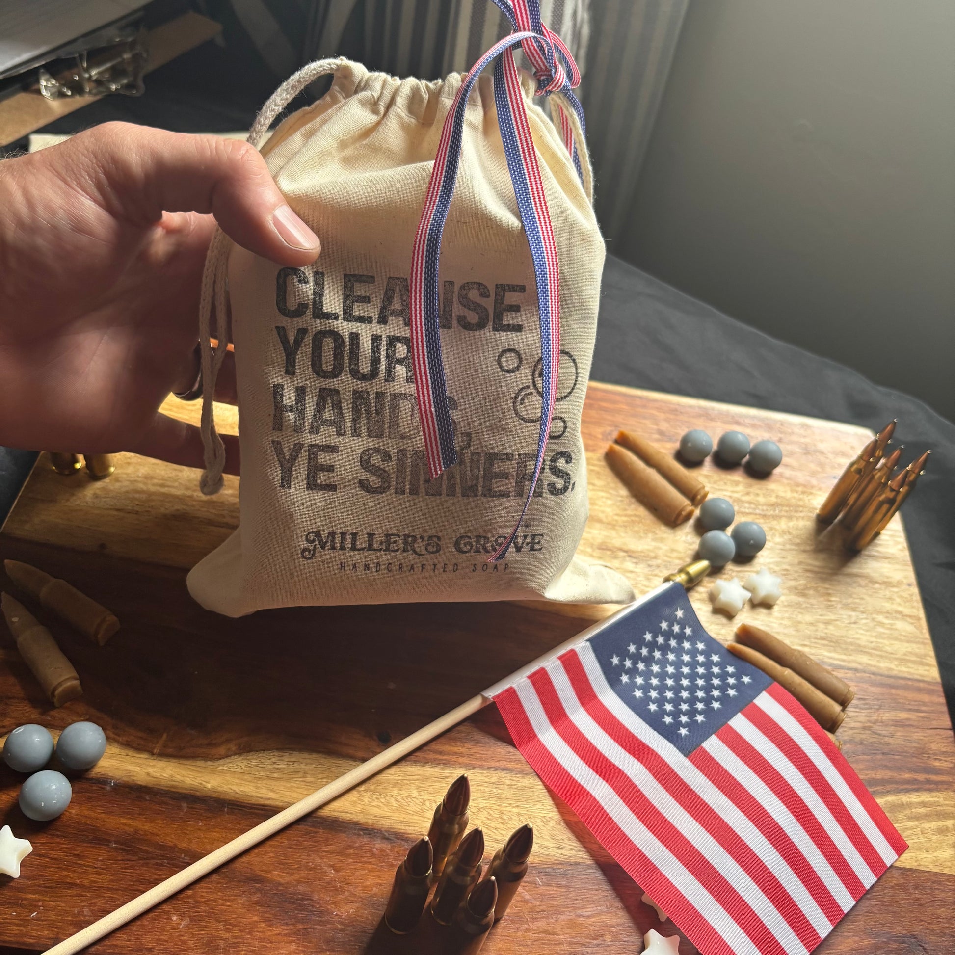 Hand holding a drawstring bag with text on a wooden surface with an American flag and various items.