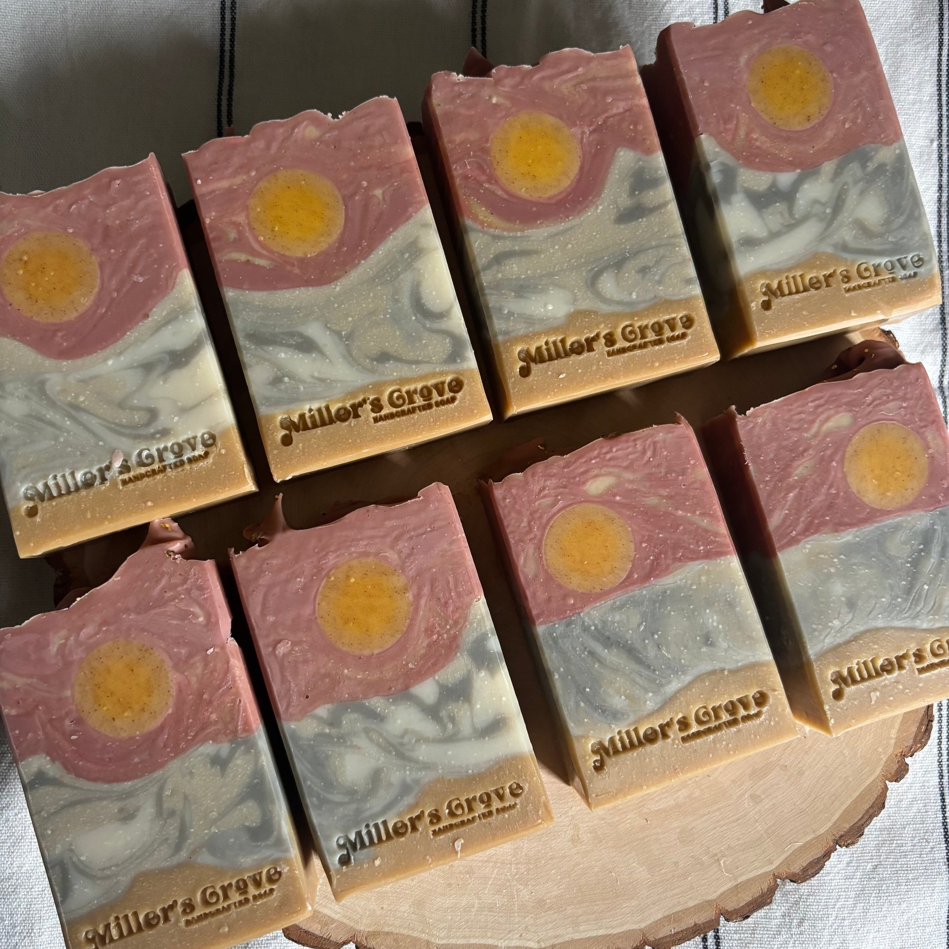 Multiple bars of soap with a sun design and 'Miller's Grove' branding on a wooden block.
