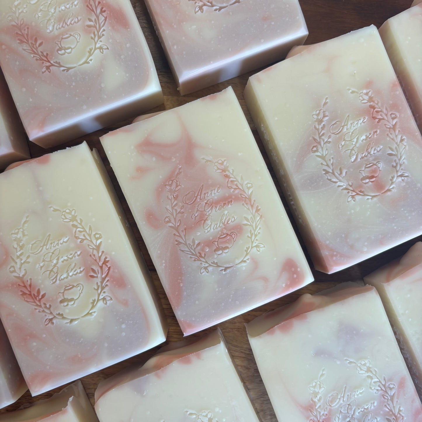 Multiple rectangular bars of handmade soap arranged on a wooden surface. The soap is off-white with soft pink swirls.