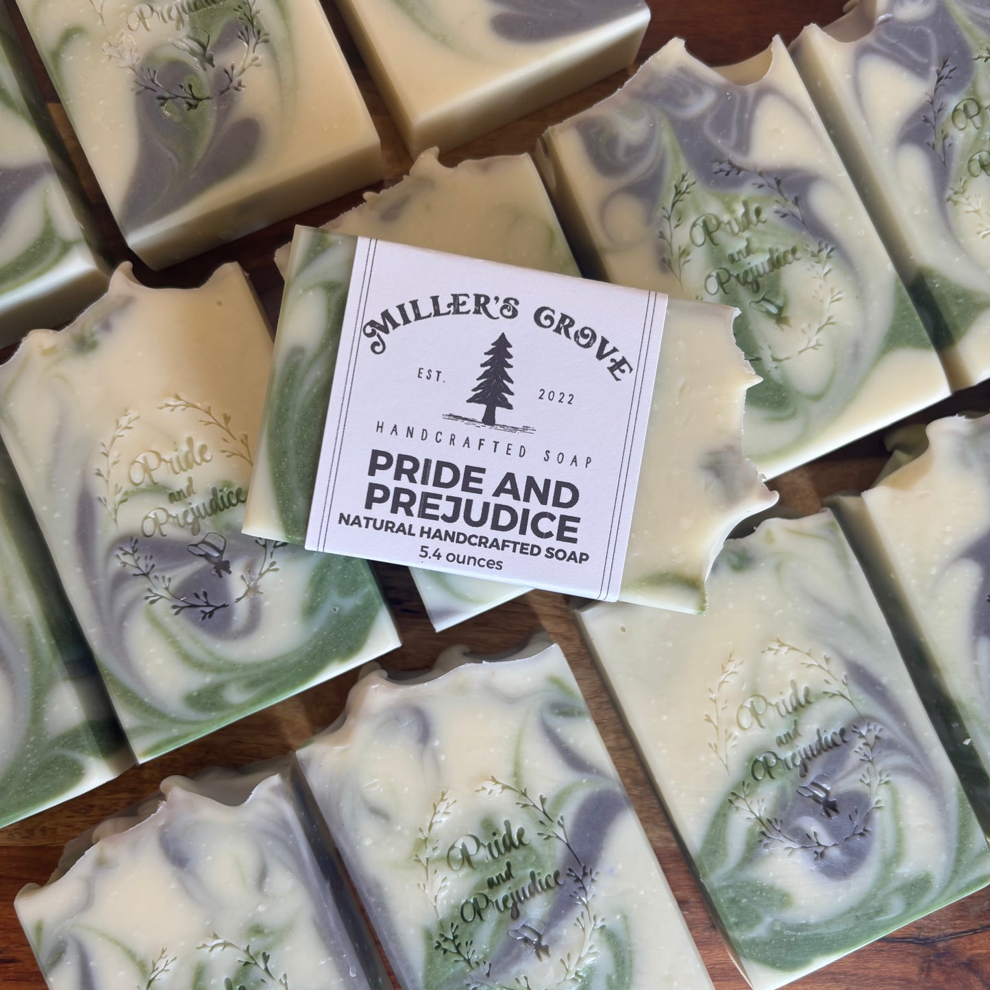 Multiple bars of Miller's Grove handmade soap with a central bar wrapped in a white paper label reading 'Pride and Prejudice Natural Handcrafted Soap 5.4 ounces.