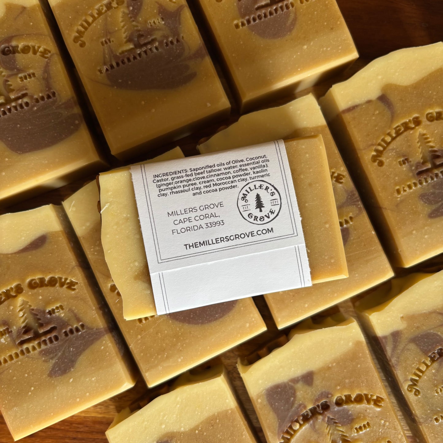 Handcrafted artisanal soap bars in a warm tan and brown marbled pattern, arranged on a wooden surface with a white paper label in the center.