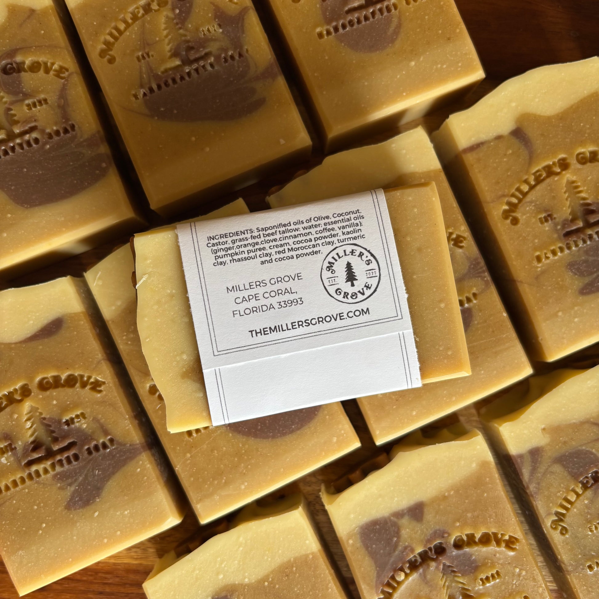 Handcrafted artisanal soap bars in a warm tan and brown marbled pattern, arranged on a wooden surface with a white paper label in the center.