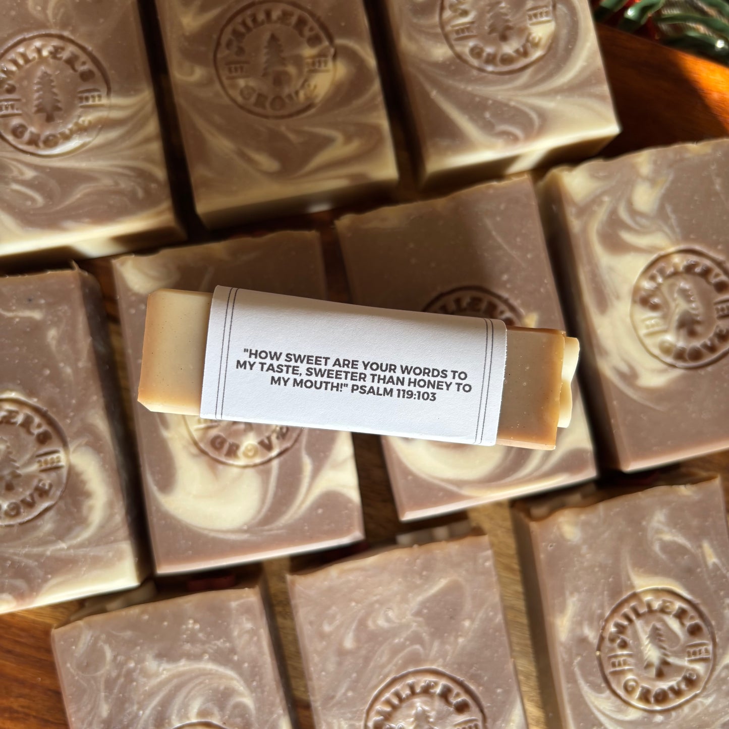 A close-up overhead view of multiple artisanal soap bars with a single wrapped bar in the center featuring a printed quote label. The soaps have a marbled cream and brown swirl pattern, and the brand name 'Miller's Grove' is embossed on the top of each bar.