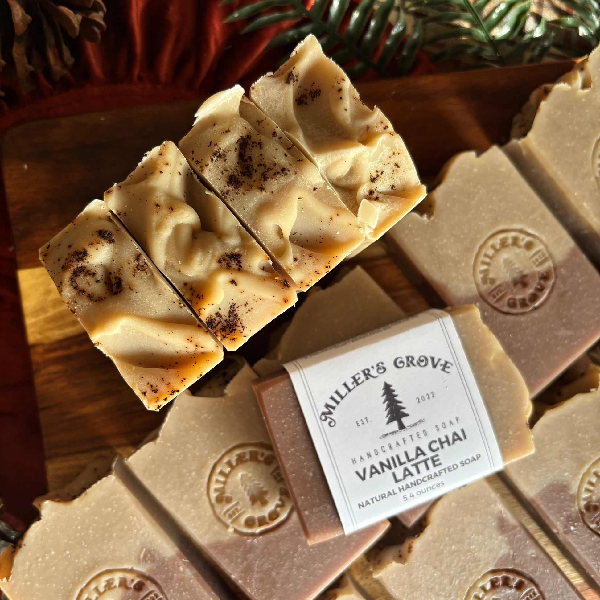Handmade vanilla chai bar soap bars arranged on a wooden board, with one bar wrapped in a paper label reading 'miler's Grove Vanilla Chai Latte Natural Handmade Soap'.